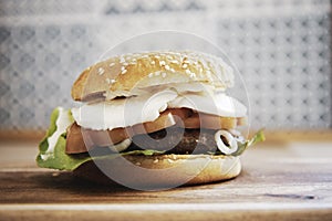 Caprese style hamburger topped with slices of fresh mozzarella cheese, tomato, basil leaves, and lettuce on toasted brioche bun on