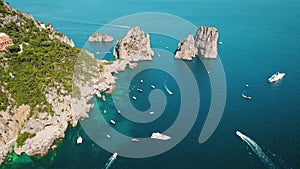 Capri Island with rocky coastline and leisure boats on Tyrrhenian Sea. Aerial view of natural landscapes and human water