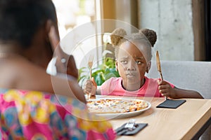 Capricious little girl with fancy hairstyle can`t wait for eating pizza.