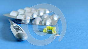 Capsule tablets and thermometer on the blue background closeup. Health care, medicine against the virus and flu