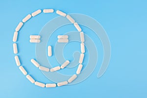 Capsules arranged in smilng face. Smiling face made from white pills on a blue background. The concept of good health. Copyspace