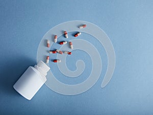 Capsules falling from the white bottle on blue paper background