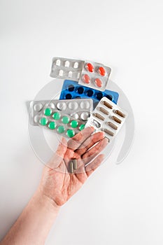 Capsules in a female hand on a background of colorful pills and capsules in blister packs on a white background. Coronavirus.