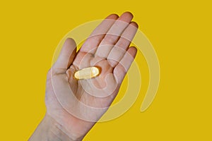 Capsules of fish oil in the palm of a person on a yellow background