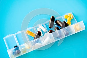 Capsules lie in a pill box on a blue background. Box for packing tablets for a week