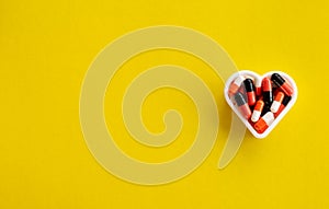 Capsules of medicine located in the shape of a heart on the right on a yellow background with an empty place for text, top view