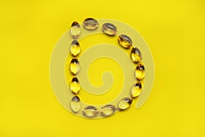 Capsules pill vitamin in the shape of the letter D on yellow background. Fish oil, vitamine d, dietary supplement, sunshine