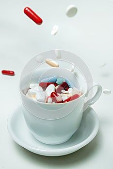 Capsules and pills fall into a mug on a white desk.