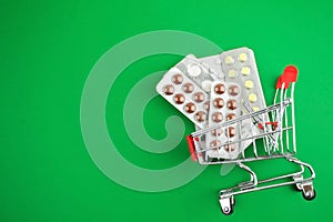 Capsules,pills,medicines in blisters on green background in shopping cart.