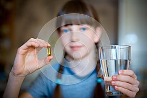 Capsules, pills in one hand, a glass of water in the other. The girl is holding the medicine in front of her. Close-up