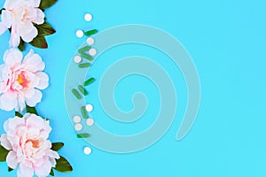 Capsules, pills and tablets with flowers on a blue table background. Top view, copy space, flat lay.