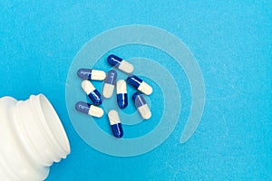 capsules & x28;pills& x29; were poured from a white bottle on a blue background. Medical background, template