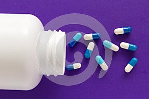 Capsules spilling out of white bottle. Purple background.