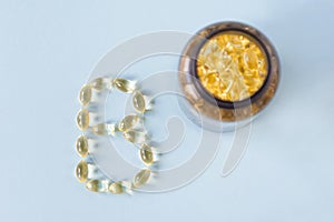 The capsules are on the surface in the form of the letter B next to the can with vitamins on a blue background.