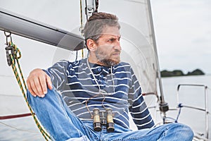 Captain with beard sits on deck of sailing yacht