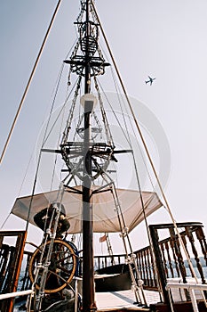 Captain at the helm of a wooden schooner sailing on the sea against the backdrop of an airplane flying in the sky