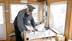 Captain of the ship is plotting the navigation route on the map in the wheelhouse.