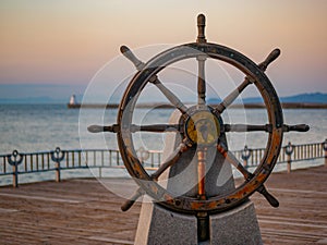 Captains steering wheel or rudder of an old wooden sailing ship in a port at sunset