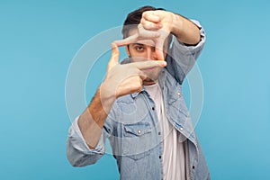 Capture moments. Portrait of inspired creative cameraman in worker denim shirt looking through photo frame