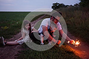 Captured in the twilight glow, a father and his children play with sparklers on a country trail