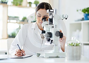 Capturing some interesting info off the sample analysed. a young scientist writing notes while using a microscope in a