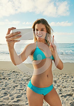 Capturing summer memories. a young woman taking a selfie while hanging out at the beach.
