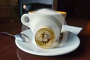 Capuccino and bitcoin gold coin on the table in cafe photo