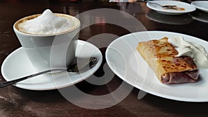 Capuccino and pancake with sour cream on the table in cafe