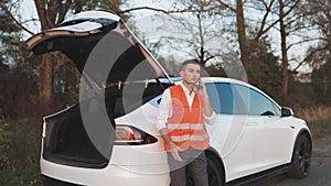 Car accident on the road. Man with reflective vest calling by phone about breakdown in her car. Emergency stop sign