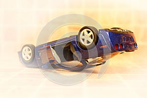 Car accident, toy car, turned upside down by wheels, road crash concept, vignette