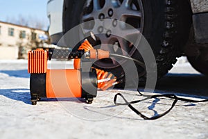 Car air compressor in working position at snow. Self-inflating wheels, automobile tire pressure control.