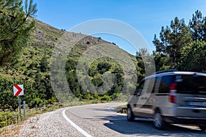 Car on asphalt island road, about to  cornering. Road lined with trees and mountains around