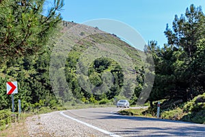 Car on asphalt island road, about to  cornering. Road lined with trees and mountains around