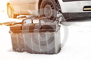 Car battery against the background of a car in winter. Winter battery discharge concept, copy space