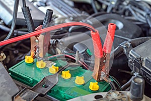 car battery clamped with black and red jumper cable to recharge