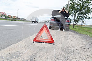 Car with a breakdown alongside the road, man sets the warning triangle