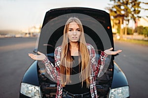 Car breakdown, sad female driver against open hood