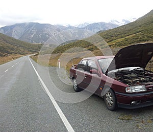 Car breakdown on the side of the empty road, mountains in the background