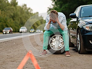 Car breakdown, tired man sitting on spare tyre