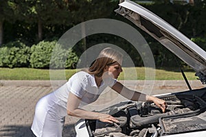 car breakdown. the woman lifted the hood of the car, bent over the engine and is trying to independently diagnose the