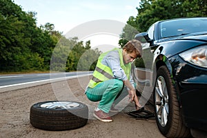 Car breakdown, young man repairing flat tyre