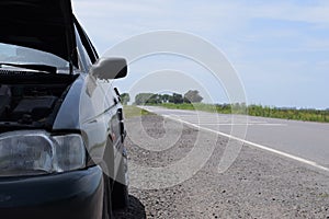 The car broke down on the road, a broken car with an open hood stands on an empty road