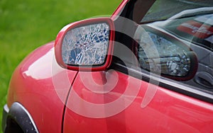 Car with broken side door mirror. Red car in green background. Asociative.