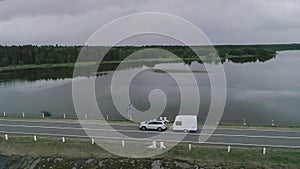 A car with a camper trailer rides along a dam across a river in Canada. Drone