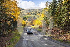 Car with canoe on dirt road in northern Minnesota below hills with trees in autumn color