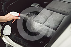 Car care concept, detailing and cleaning car interiors. Worker spraying cleaning solution on car upholstery