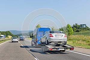 Car carrier trailer with car. Blue minibus with tow truck transporter carrying car on highway