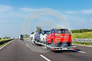 Car carrier trailer with new blue white and red car on highway