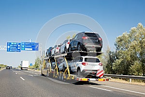 Car carrier trailer with new cars for sale on bunk platform. Car transport truck on the highway