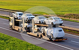 Car carrier trailer transports cars on highway on sunset background. Auto transport and car shipping services concept. Truck with